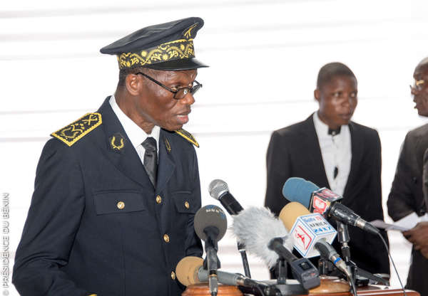 Un homme en uniforme officiel prend la parole devant plusieurs microphones lors d’un événement officiel