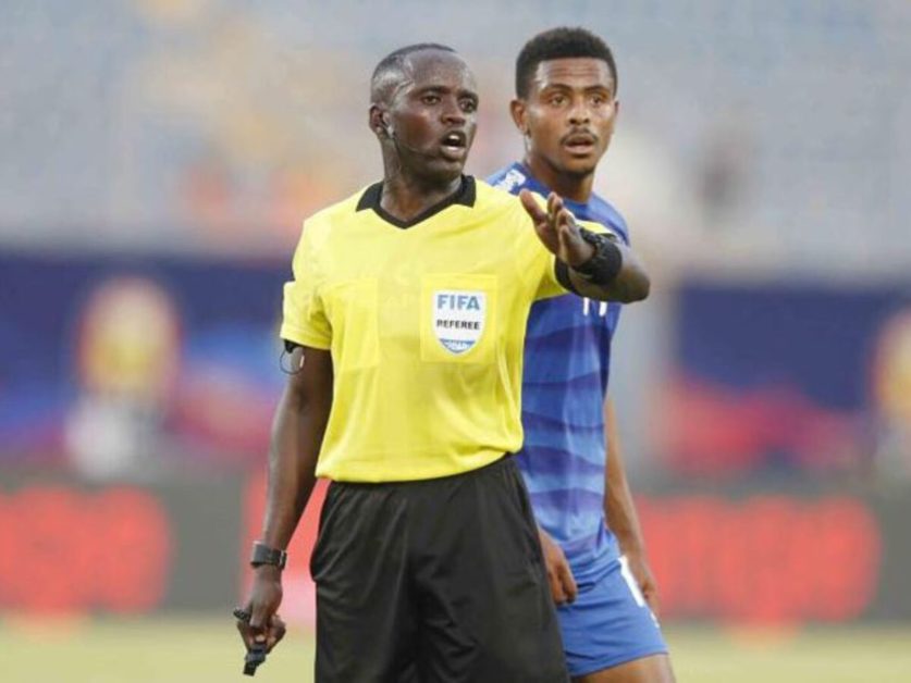 Un arbitre en maillot jaune donne des instructions à un joueur en tenue bleue lors d’un match de football