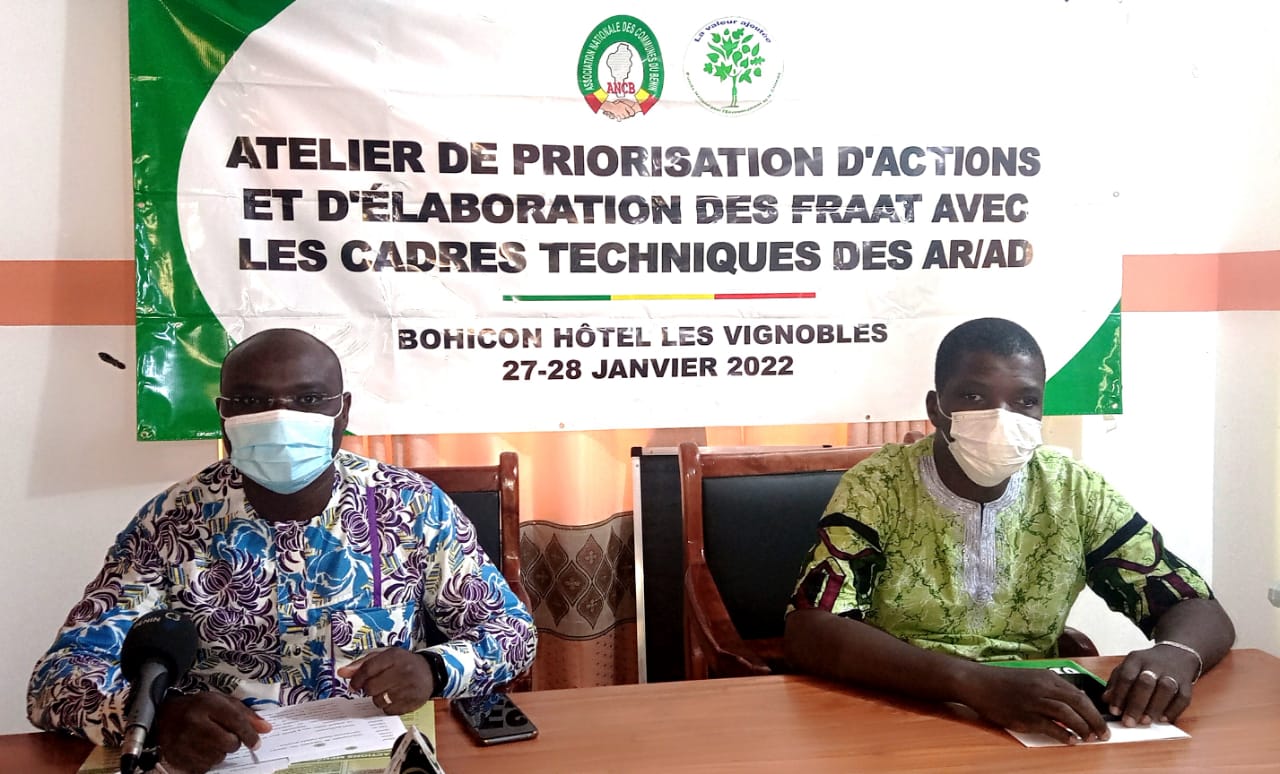 Deux hommes masqués assis à une table devant une banderole d’atelier de priorisation d’actions et élaboration de feuilles de route