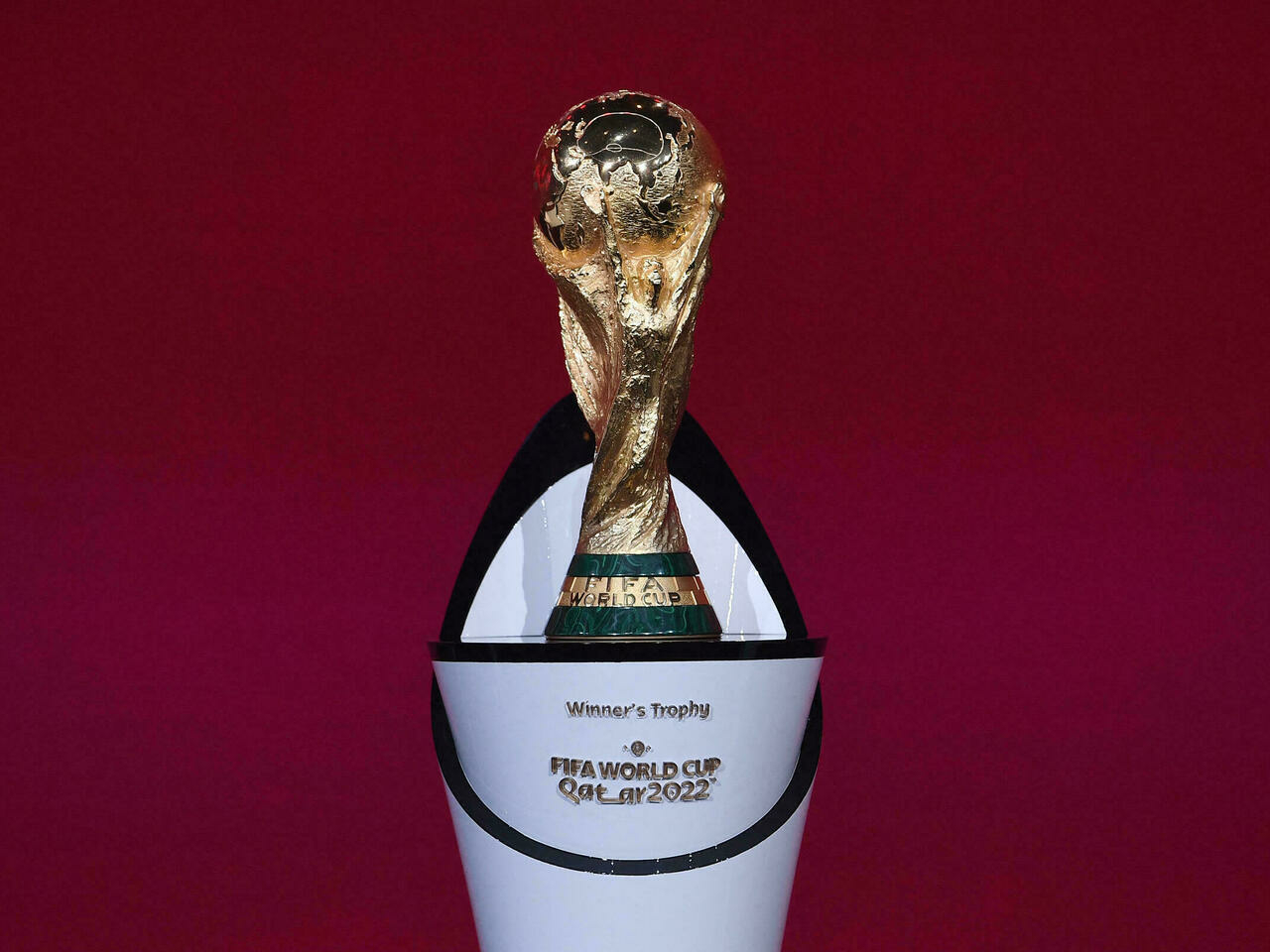 Trophée doré de la Coupe du Monde posé dans son socle blanc avec fond rouge
