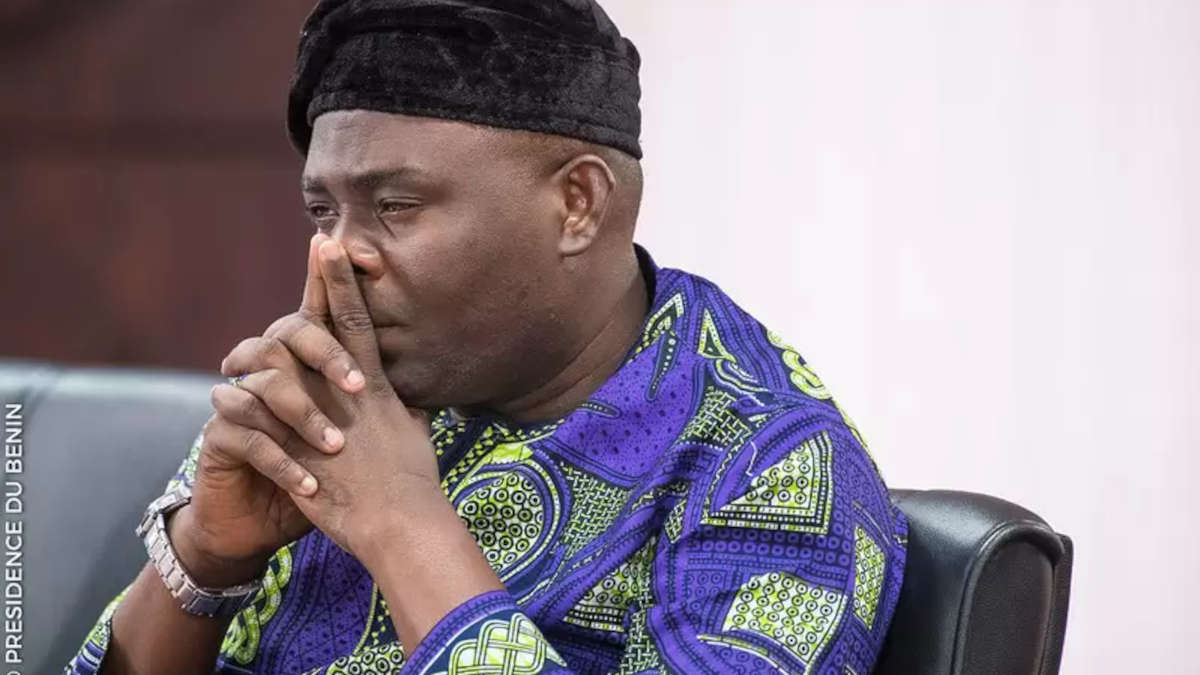 Homme portant une tenue traditionnelle colorée en position pensive les mains jointes devant le visage assis sur une chaise noire