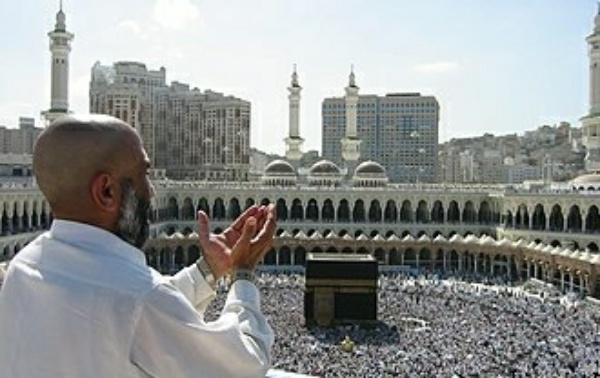 Homme en prière de dos face à la Kaaba entourée de milliers de pèlerins au centre d'une grande mosquée.
