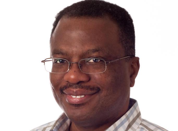 Homme souriant portant des lunettes et une chemise à carreaux sur fond blanc