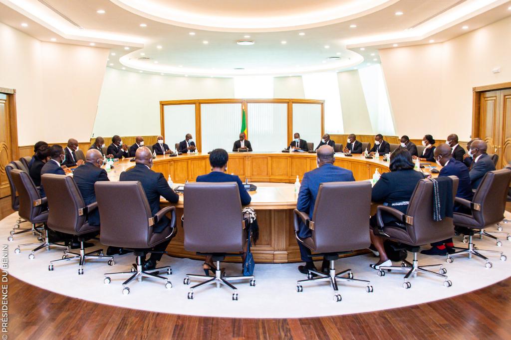 Personnes assises autour d'une grande table ronde dans une salle de réunion lumineuse avec un drapeau tricolore au centre