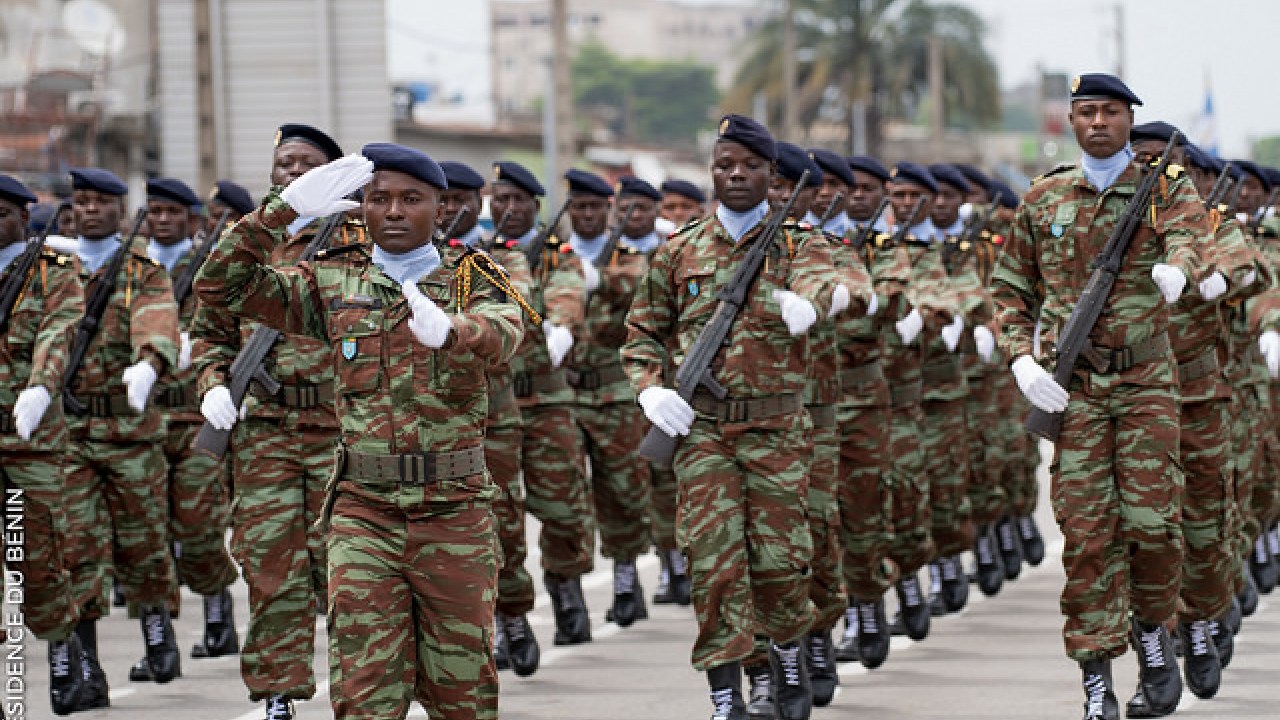 Un groupe de militaires en uniforme de camouflage défile en formation serrée dans une rue urbaine.