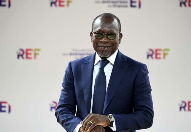 Homme en costume bleu et lunettes souriant devant un mur avec le logo coloré REF en arrière-plan