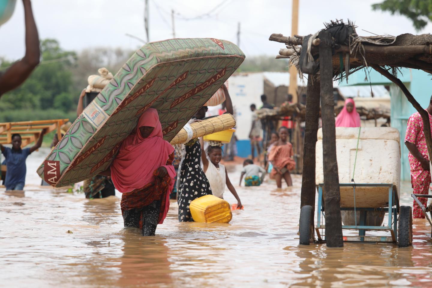 Des personnes marchent dans une rue inondée, certaines portant un matelas et des objets sur la tête pour se protéger des eaux hautes