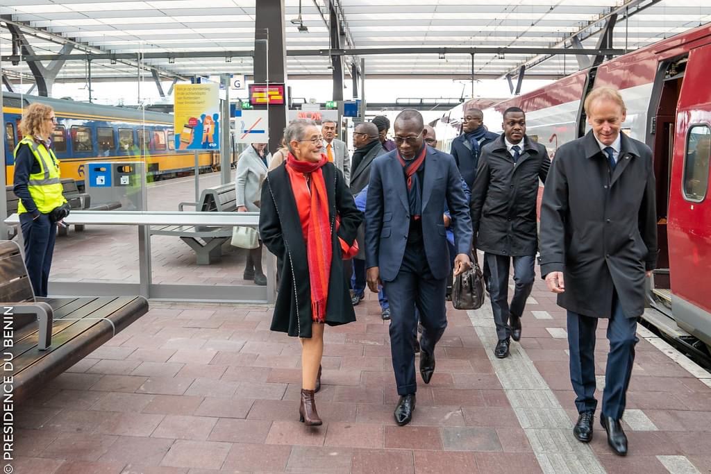 Un groupe de personnes bien habillées marche sur un quai de gare entre deux trains sous une verrière transparente