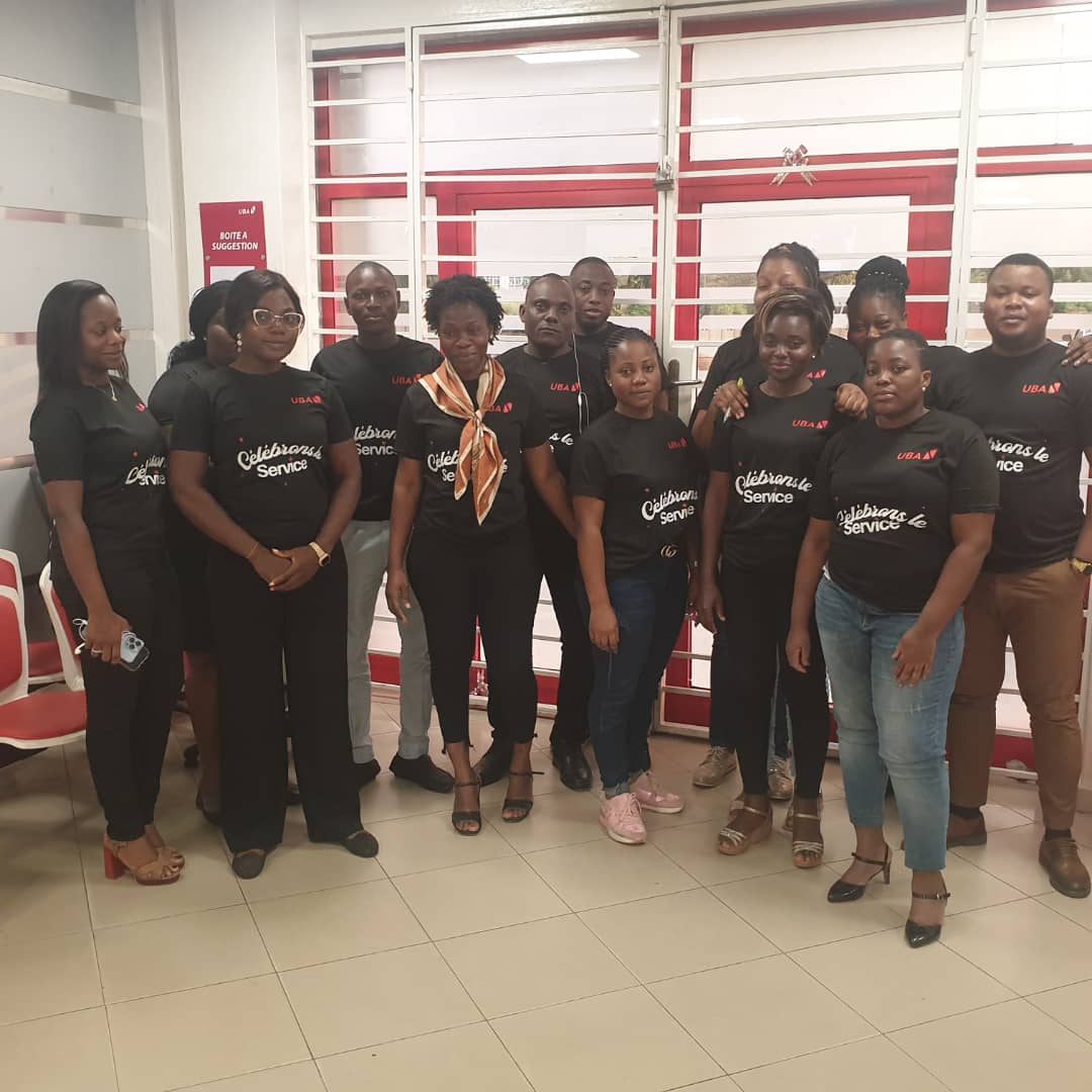 Groupe de personnes posant debout en intérieur portant des t-shirts noirs avec inscriptions rouges et blanches