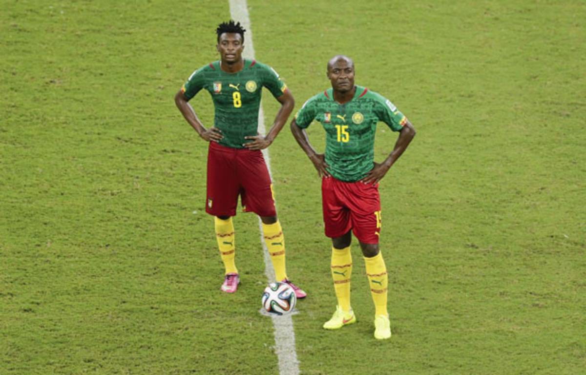 Deux joueurs de football africains en tenue verte et rouge posent sur un terrain de jeu gazonné près du ballon central
