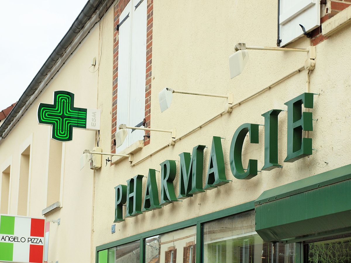 Façade d une pharmacie avec enseigne verte et croix lumineuse suspendue au mur