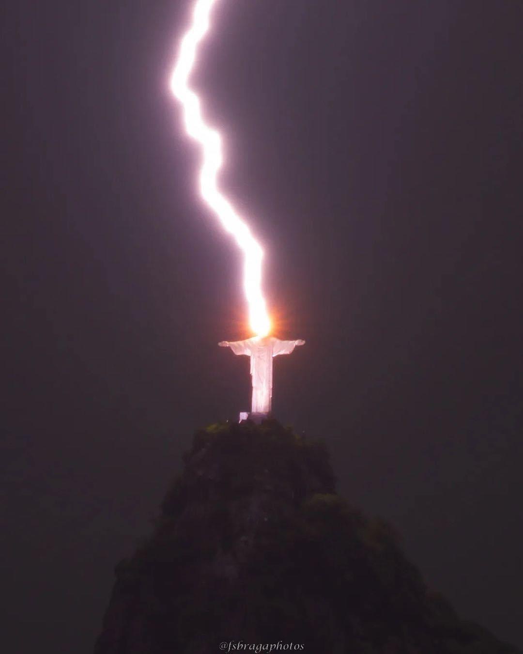 Éclair frappant simultanément une statue géante aux bras déployés sur un sommet rocheux dans la nuit