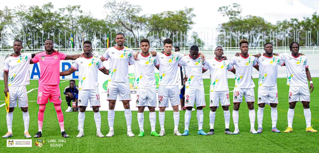 Une équipe de football en tenue blanche alignée sur le terrain avec les bras sur les épaules des coéquipiers.