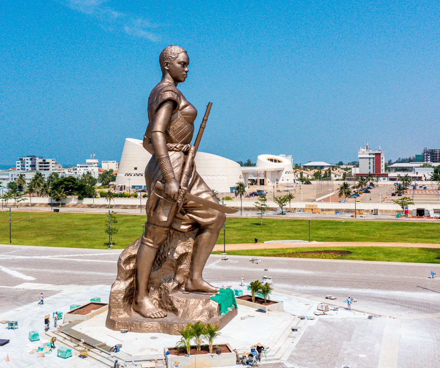 Statue monumentale d’une femme tenant un bâton sur une grande place avec bâtiments modernes en arrière-plan