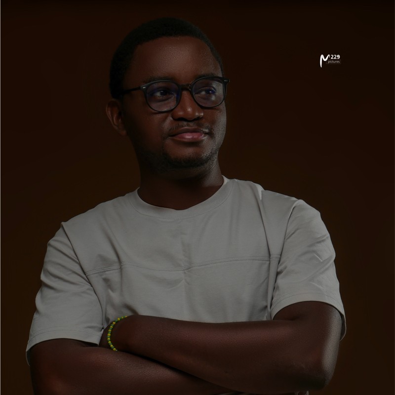 Homme portant des lunettes et un t-shirt clair, bras croisés, regard dévié, fond sombre