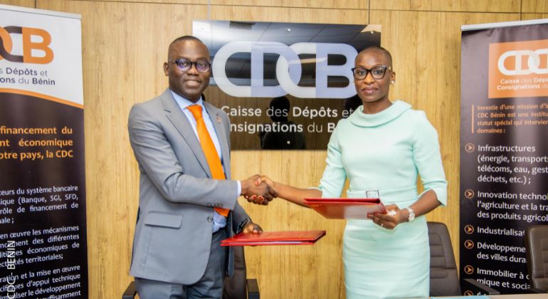 Deux personnes en costume échangent un document devant un panneau avec le sigle CDCB dans un bureau.
