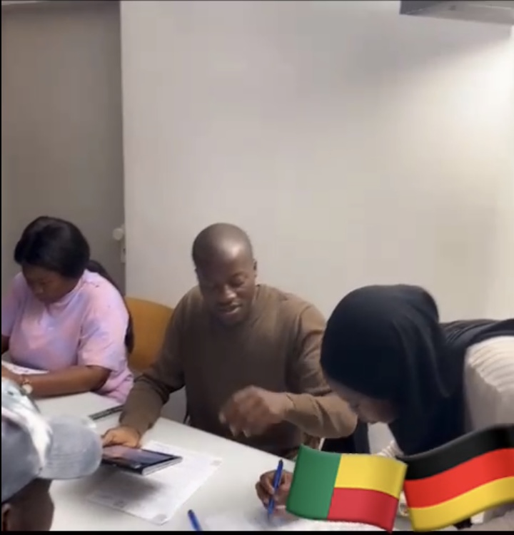 Trois personnes assises à une table écrivent et manipulent des documents dans une salle simple