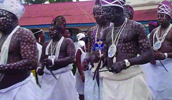 Des hommes au corps peint et ornés de bijoux portent des pagnes blancs lors d'une cérémonie traditionnelle en extérieur