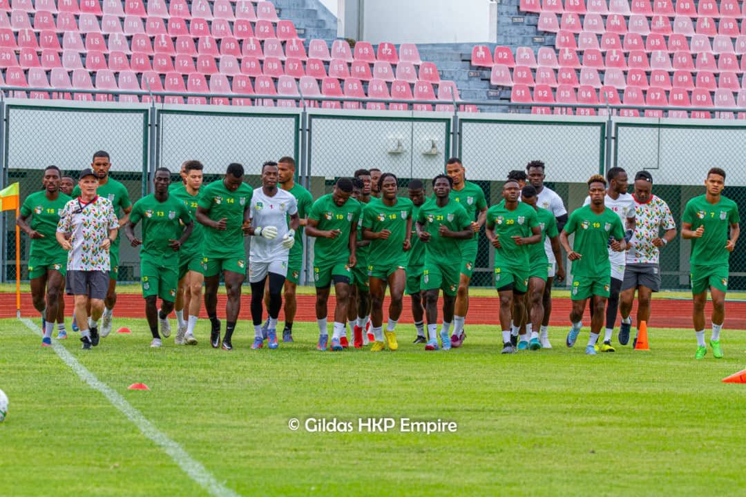 Une équipe de joueurs en tenue verte court sur un terrain de football entouré de gradins vides rouges