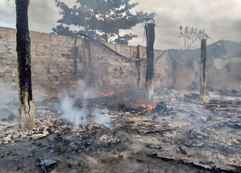 Terrain ravagé par un incendie avec des débris brûlés encore fumants et des piliers carbonisés d’une structure détruite