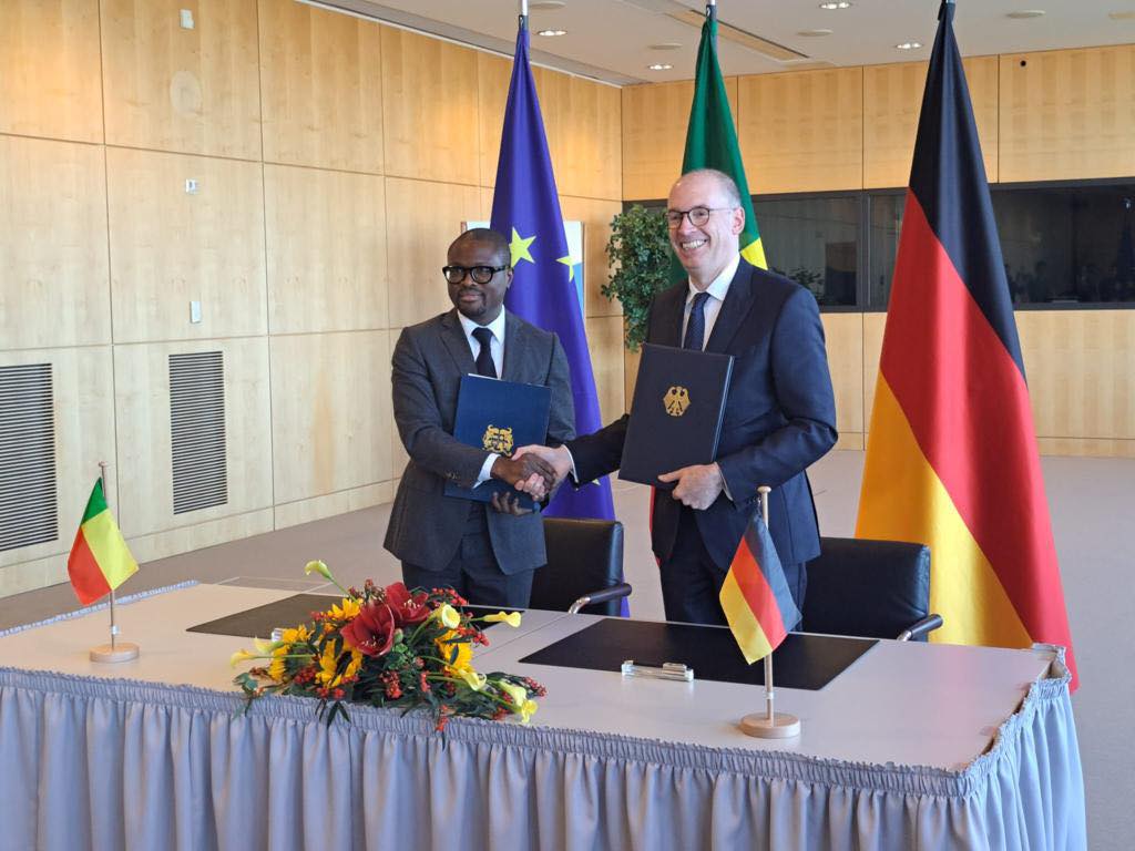 Deux hommes en costume échangent une poignée de main devant des drapeaux européens et nationaux avec un bouquet de fleurs sur une table recouverte d'une nappe g