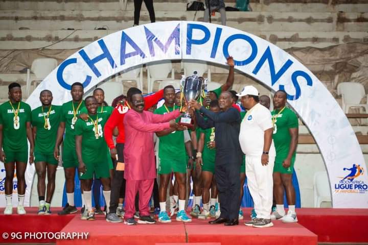 Joueurs en tenue verte fêtant la victoire avec un trophée devant une arche blanche marquée « CHAMPIONS
