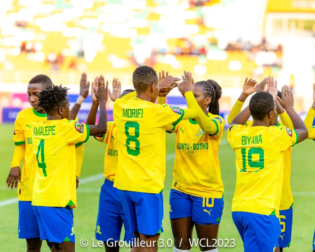 Joueuses en maillots jaunes et shorts bleus se félicitant par des accolades sur un terrain de football