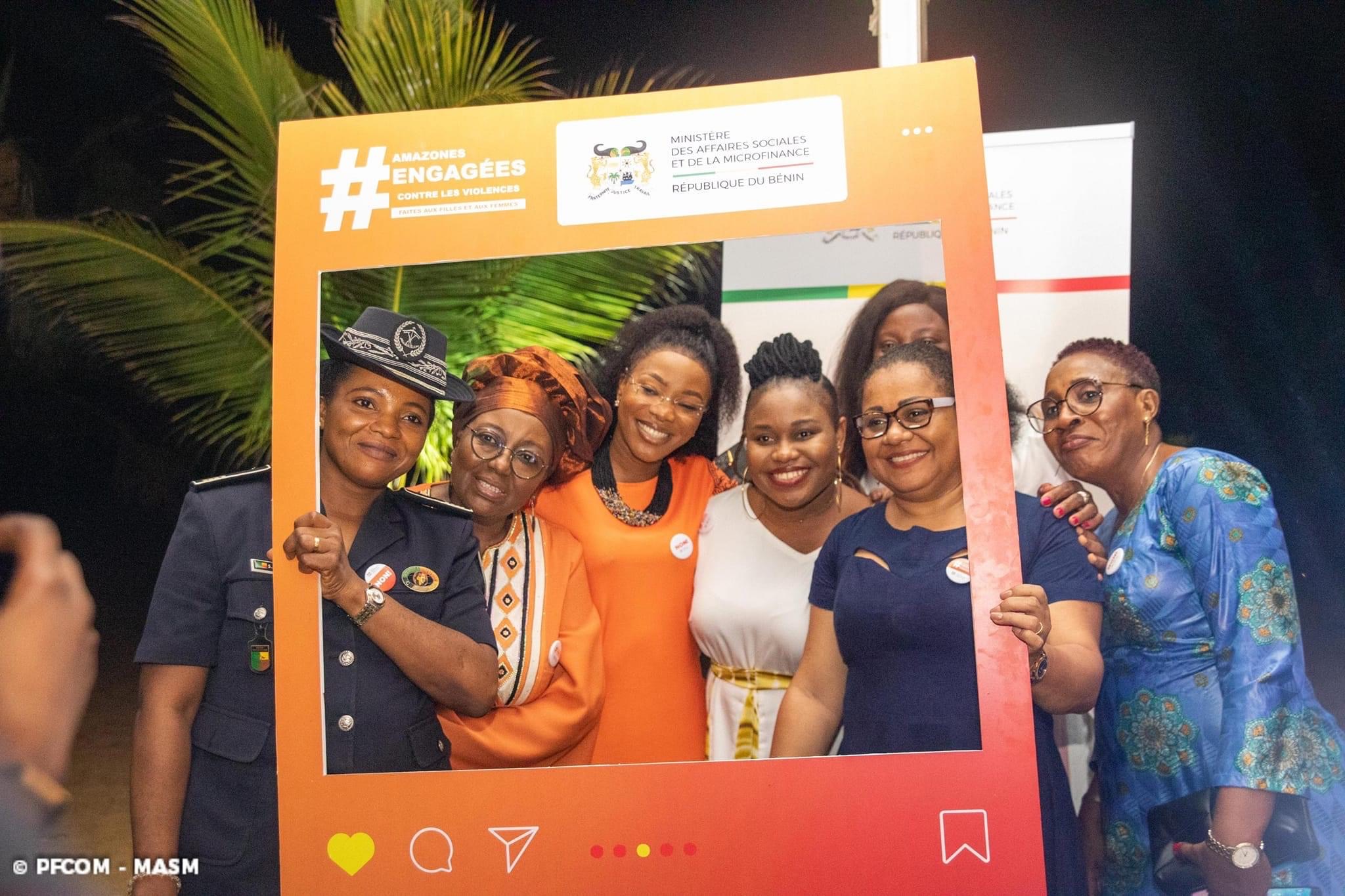 Groupe de femmes souriantes, dont une en uniforme policier, posant derrière un cadre orange avec hashtags et logos officiels