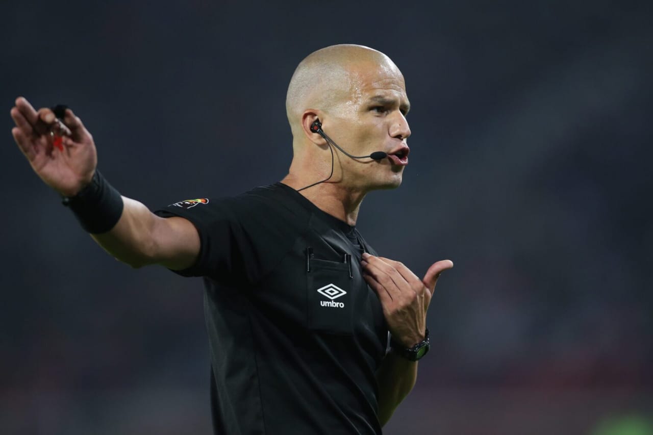 Arbitre en tenue noire avec micro et oreillette gesticule pendant un match de football