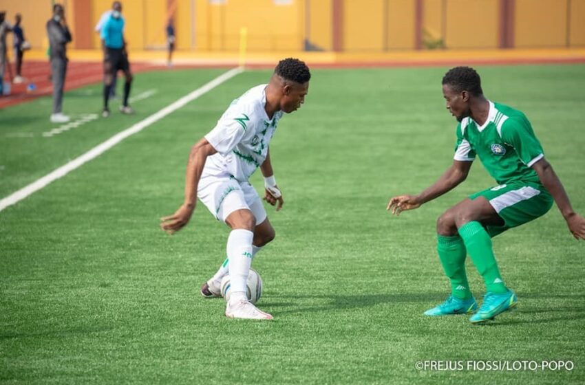 Deux joueurs en tenue de football se disputent le ballon sur un terrain en gazon synthétique lors d’un match