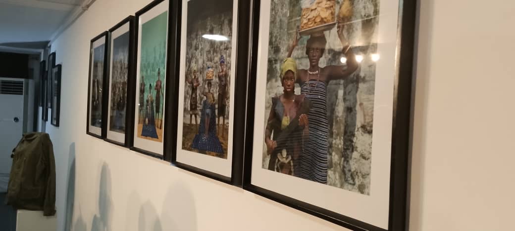 Photographies encadrées accrochées sur un mur blanc avec des silhouettes et un manteau suspendu sur la gauche