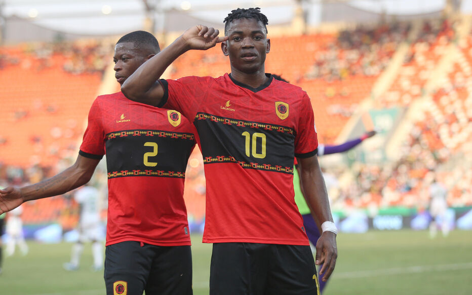 Deux joueurs de football en maillot rouge et noir célèbrent sur le terrain devant un stade rempli de spectateurs