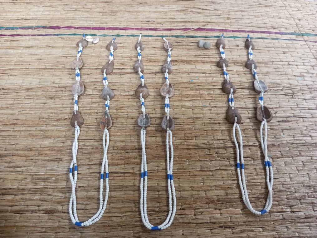 Quatre chaînes de perles blanches et bleues ornées de cauris posées sur un tapis en paille tressée