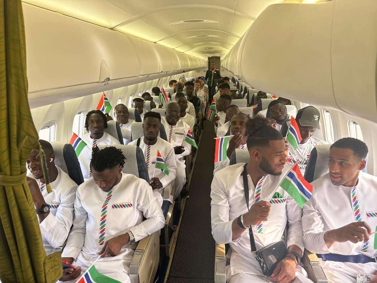 Des hommes vêtus de blanc tiennent de petits drapeaux aux couleurs rouge, bleu et vert assis dans un avion