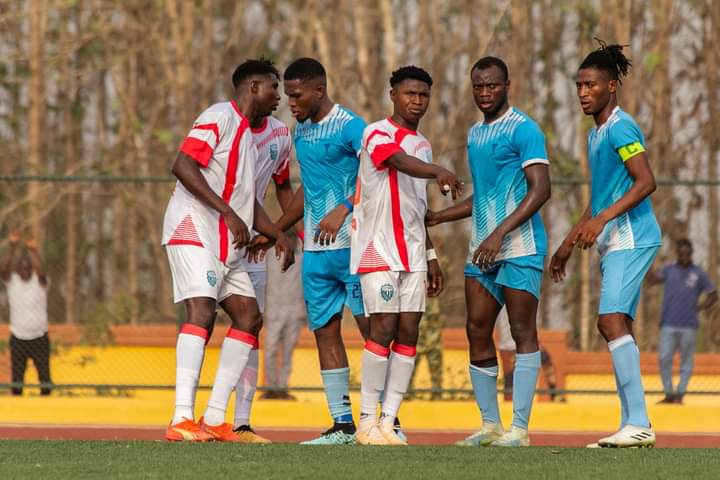 Cinq joueurs de football en tenue discutent et se tiennent sur un terrain pendant un match sous un ciel clair