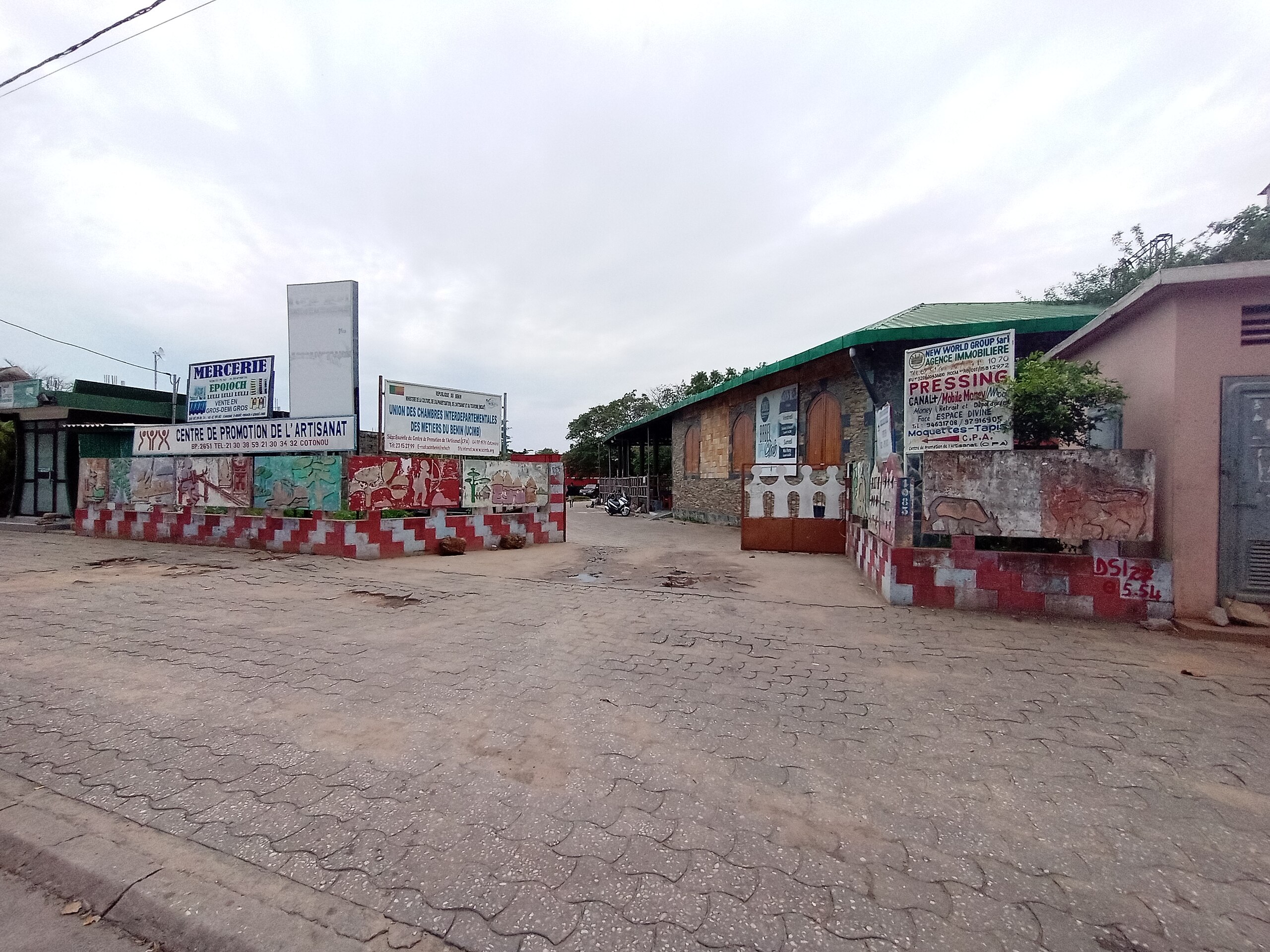 Entrée avec pancartes publicitaires sur mur et sol pavé sous ciel nuageux