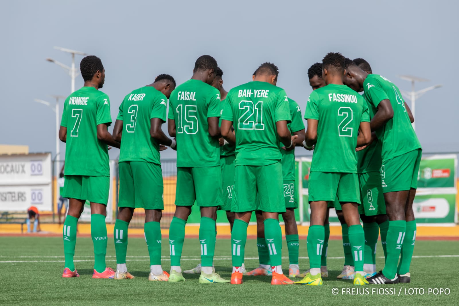 Joueurs de football en cercle bras dessus bras dessous en maillot vert sur un terrain de football