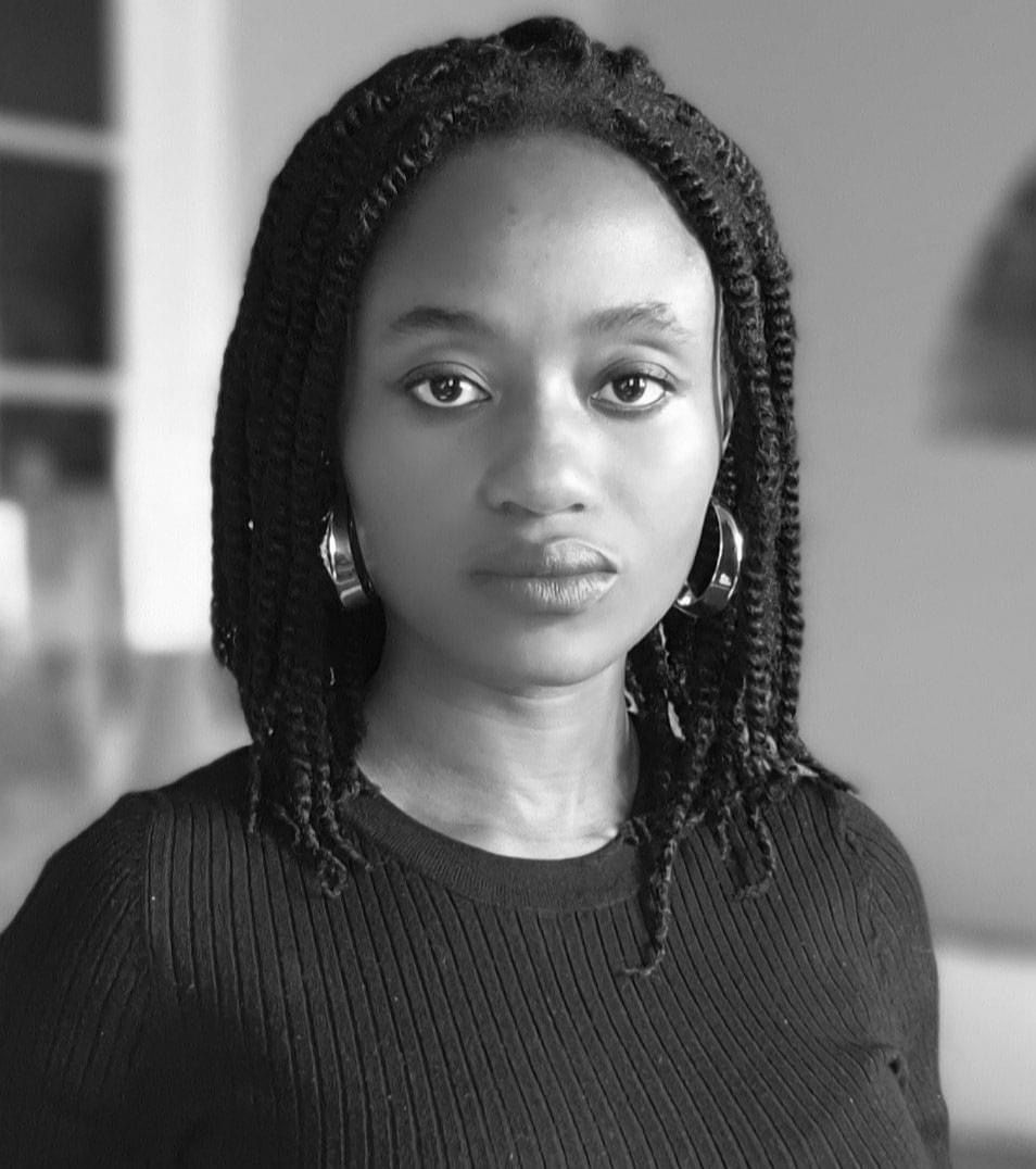 Jeune femme au regard droit portant un pull noir et des boucles d’oreilles métalliques avec des cheveux tressés.