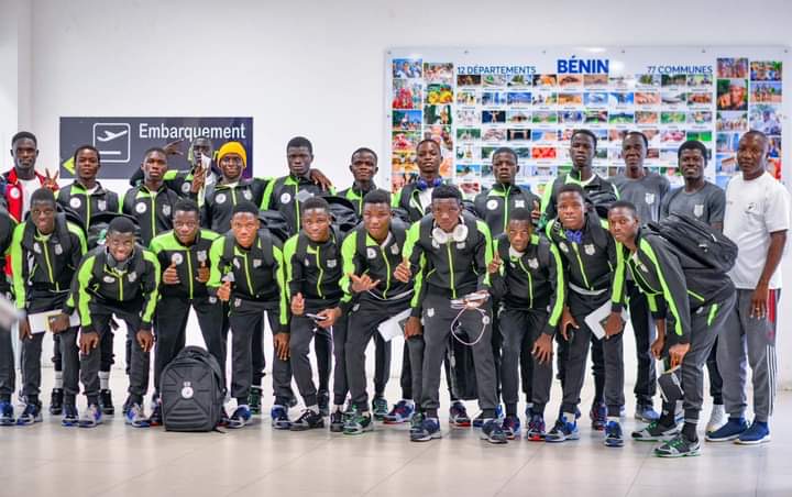 Jeunes hommes en tenue de sport noire et verte posant en groupe devant un mur d affiches colorées dans un hall d embarquement