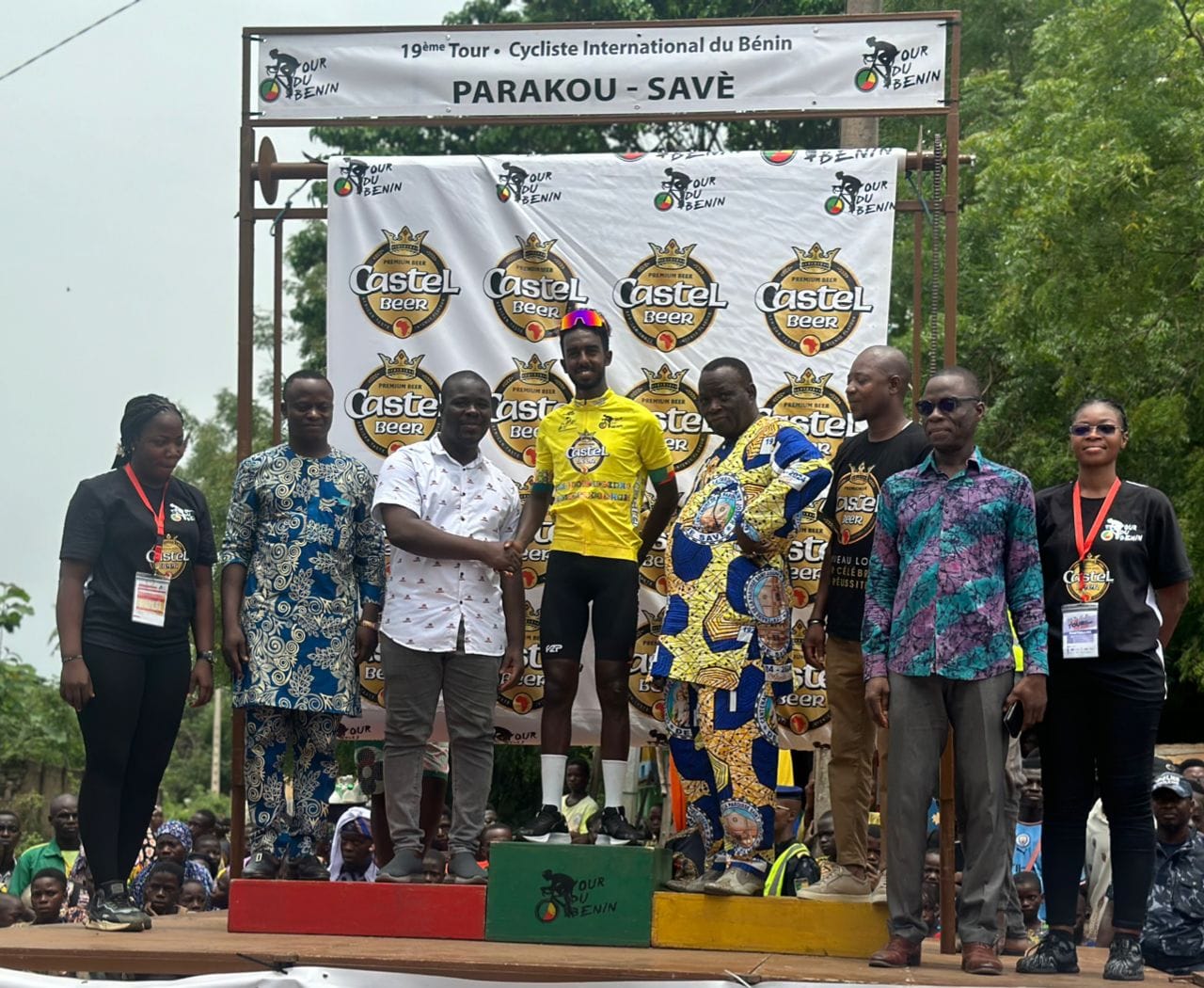 Un coureur en maillot jaune est félicité sur un podium entouré de plusieurs personnes lors d’une cérémonie officielle
