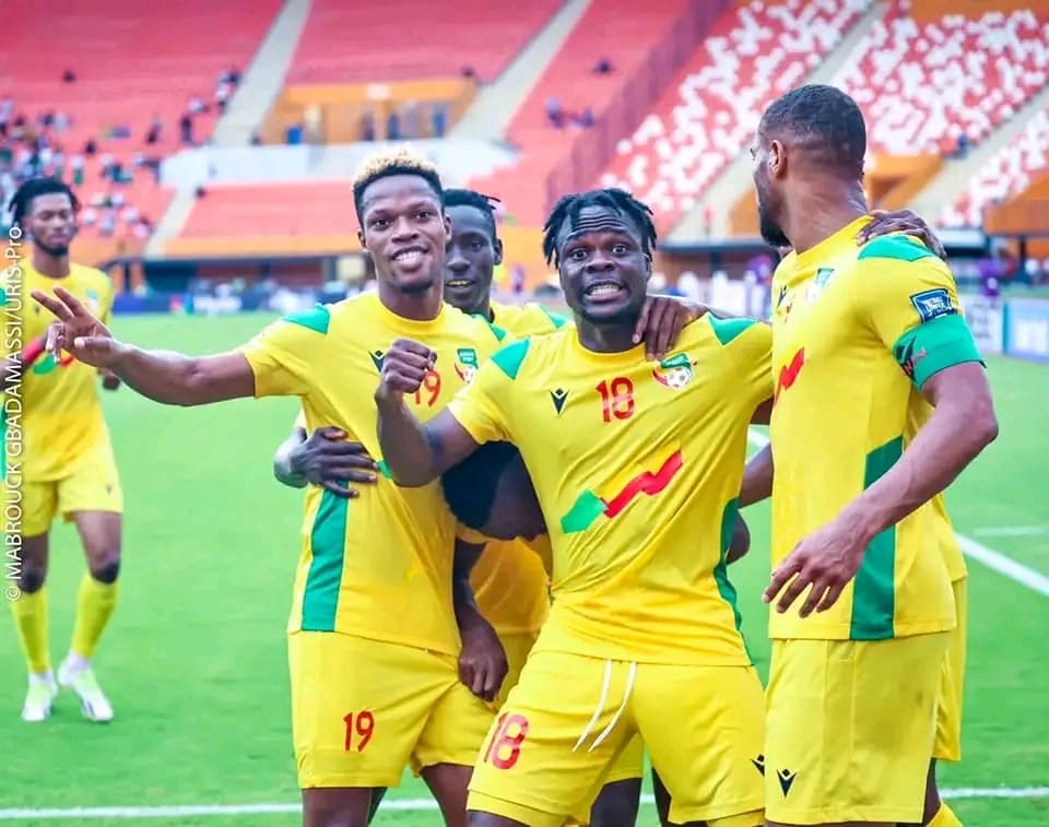 Des joueurs de football en maillot jaune célèbrent un but sur un terrain de stade avec tribunes vides en arrière-plan