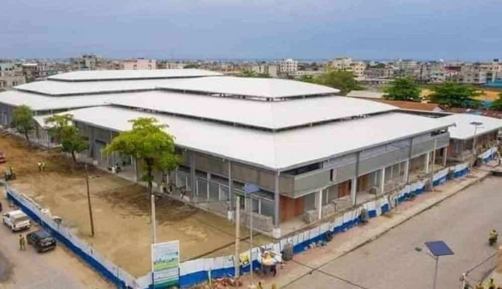 Grand bâtiment moderne avec toiture blanche dans une zone urbaine entouré de rues et de quelques véhicules stationnés