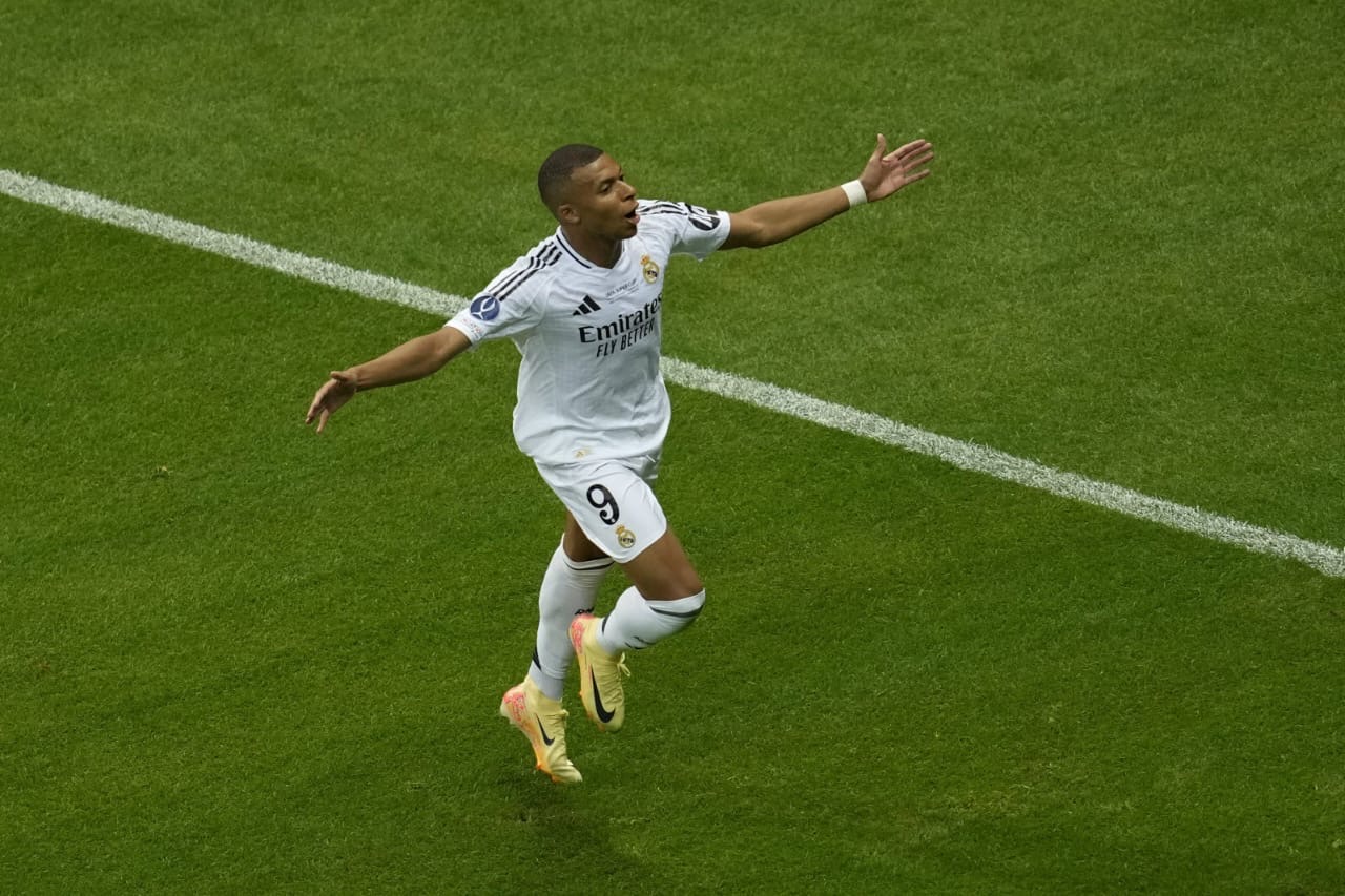 Un joueur de football en maillot blanc célèbre un but sur un terrain vert près de la ligne de touche