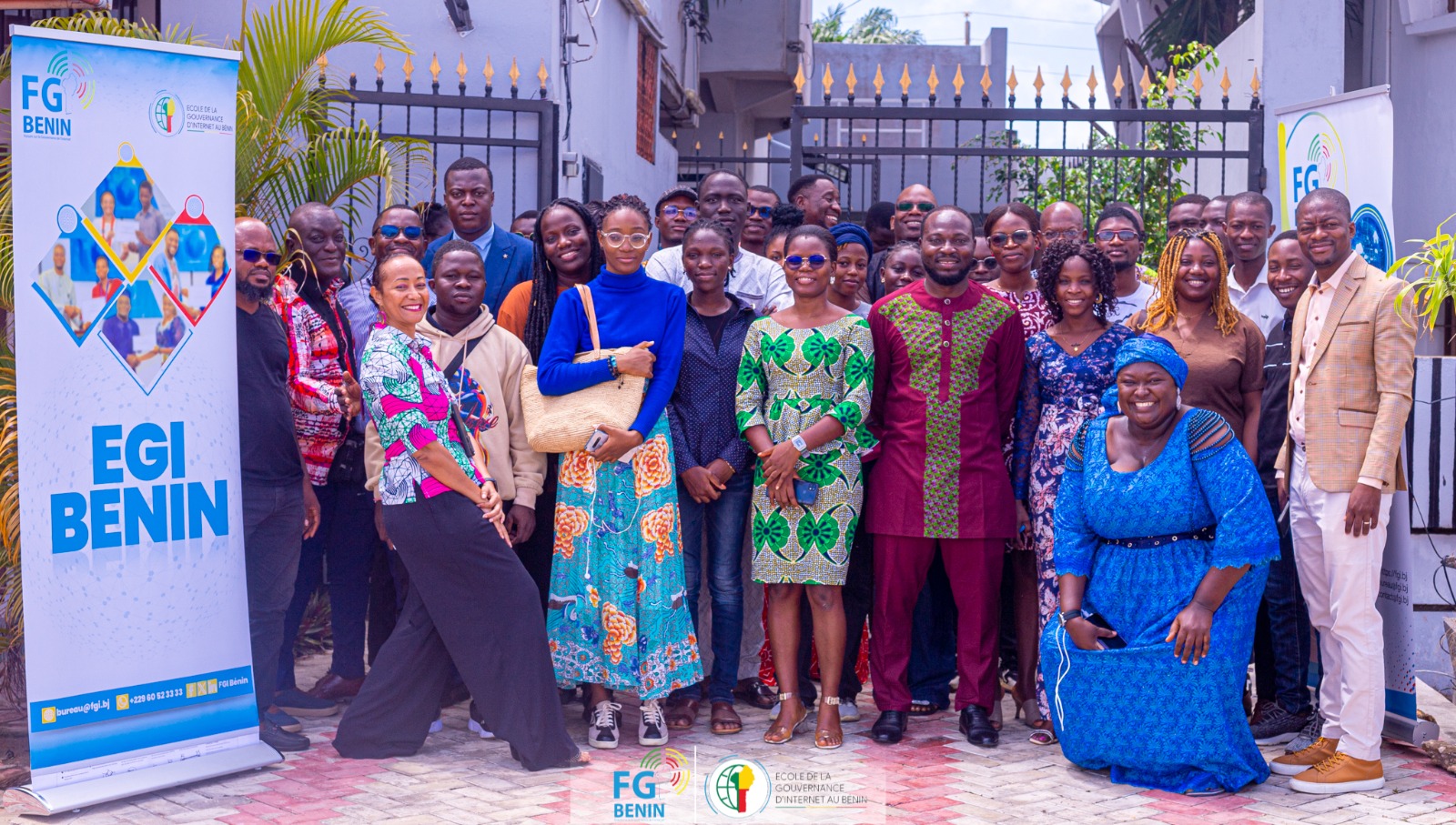 Groupe de personnes posant devant une entrée avec deux panneaux FG BENIN de chaque côté