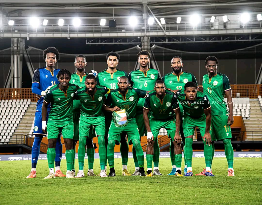 Onze joueurs de football en tenue verte posant sur un terrain de stade vide sous des projecteurs allumés