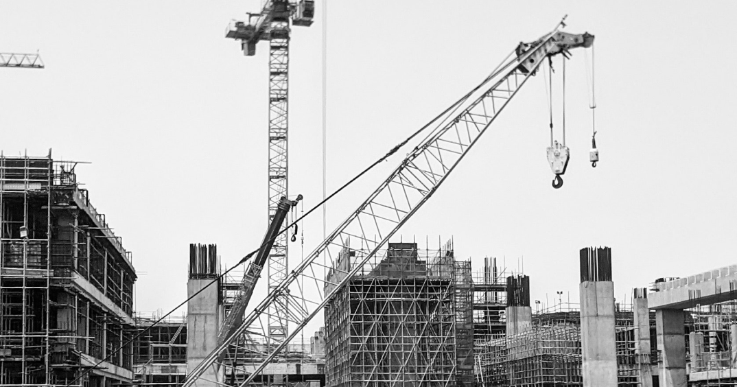 Grue de chantier au centre d’un vaste site avec plusieurs structures en béton en construction et échafaudages.