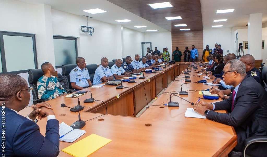Plusieurs personnes assises autour d’une grande table de réunion dans une salle avec microphones et dossiers devant elles