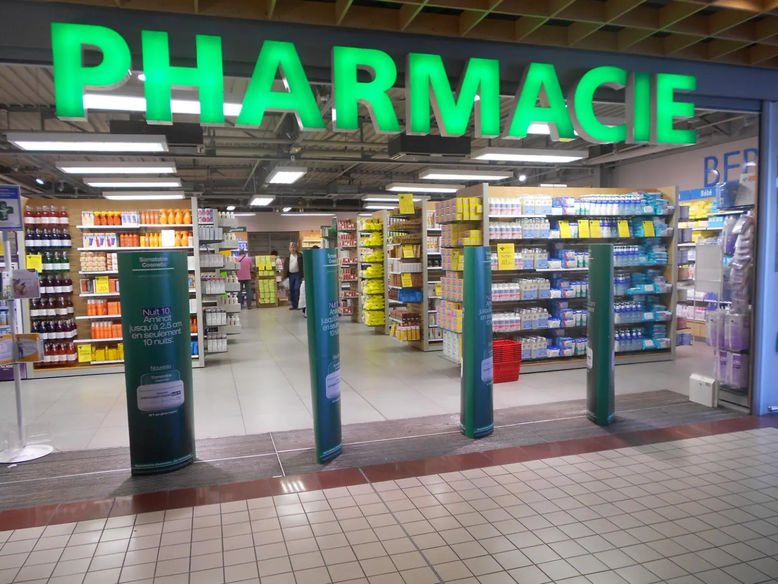 Grand espace intérieur avec rayonnages remplis de produits de santé et enseigne lumineuse verte PHARMACIE au-dessus de l'entrée