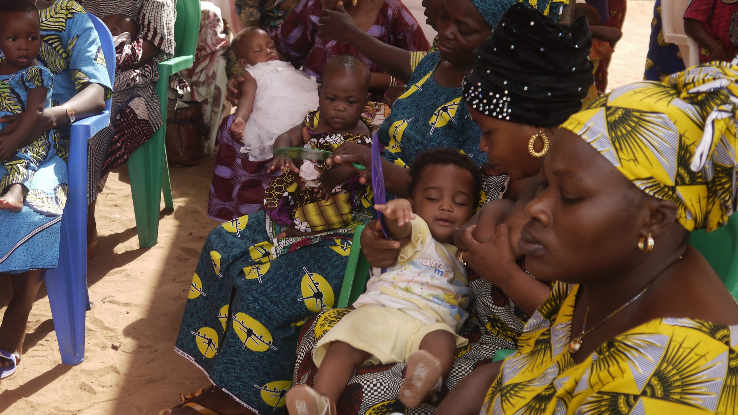 Des mères assises avec leurs bébés dans un rassemblement en plein air sous un soleil éclatant