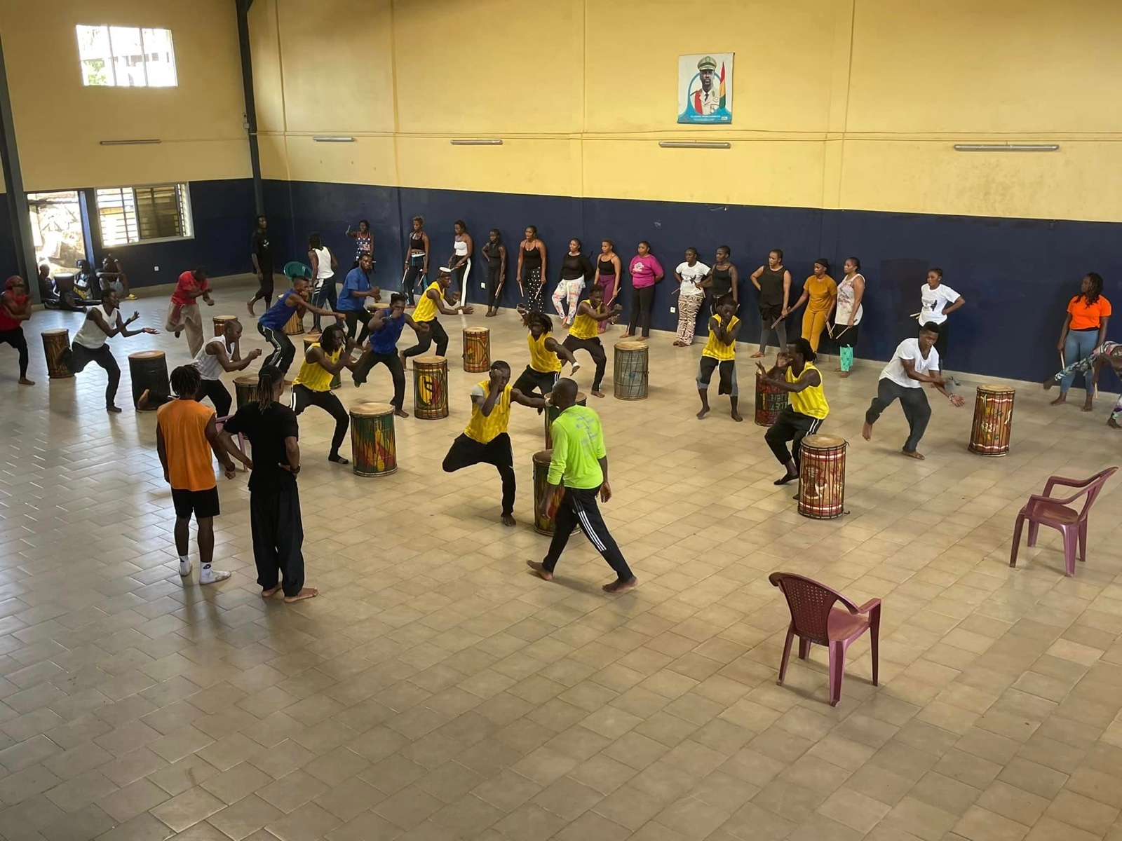 Jeunes en tenue de sport dans une salle effectuent une danse rythmée autour de djembés disposés en cercle